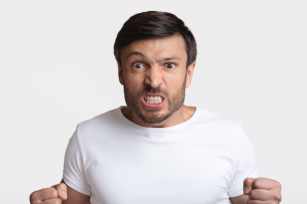 Furious man clenching fists in rage on white studio background