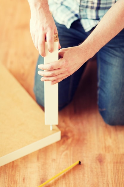 furniture, home and moving concept - close up of male hands assemblying legs to table