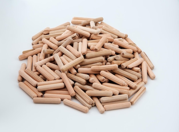 Furniture wooden dowels are stacked in a small round pile and isolated on a gray background with slight shadows.