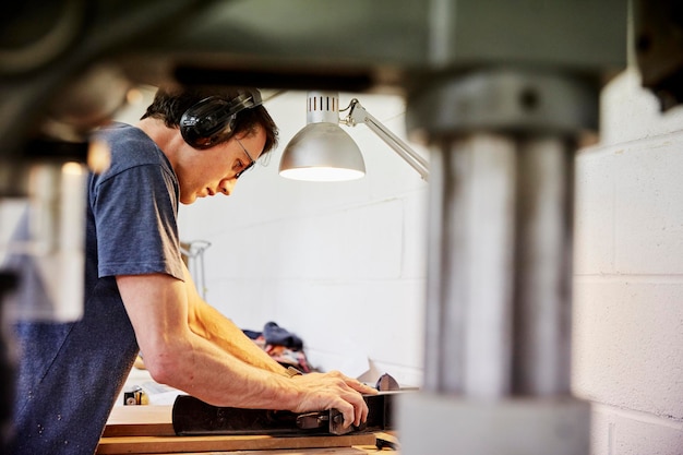 A furniture workshop making bespoke contemporary furniture pieces using traditional skills in modern design A man in ear defenders holding wood using a machine