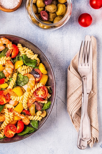 Fusili pasta salad with shrimps, tomatoes, peppers, spinach, olives