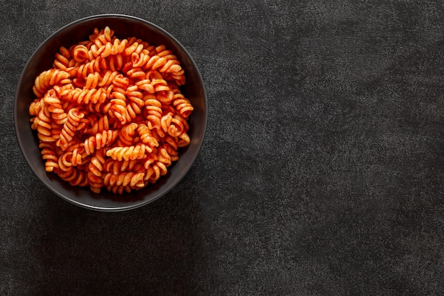 Fusilli cooked pasta with tomato sauce on dark background top view space to copy text