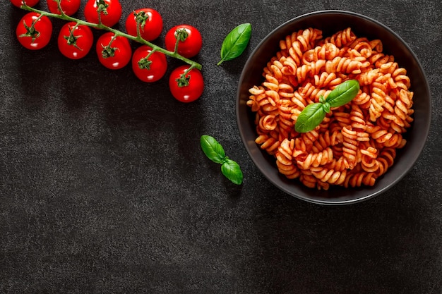 Fusilli cooked pasta with tomato sauce tomatoes cherry and basil leaf on dark background top view space to copy text