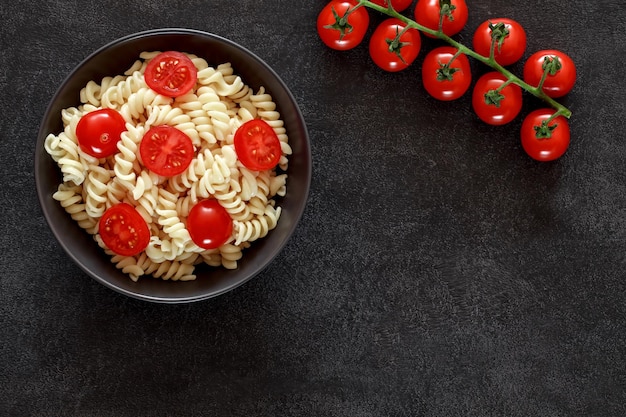 텍스트를 복사하기 위해 어두운 배경 상단 보기 공간에 토마토 체리와 함께 Fusilli 요리 파스타