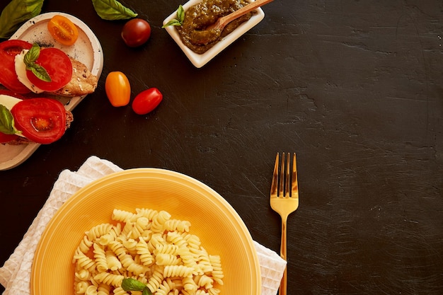 Fusilli pasta caprese salad with tomato basil mozzarella appetizer with pesto on black rustic background Top view food Italian dinner Copy space