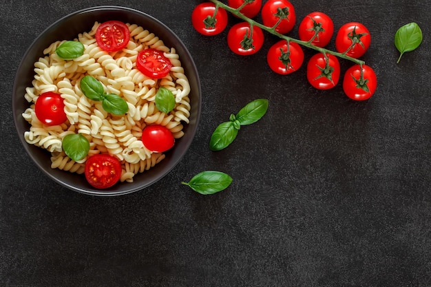 Fusilli pasta cooked with tomato and basil cherry tomatoes branch on dark background top view space to copy text