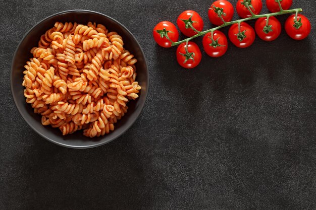 Fusilli pasta cooked with tomato sauce branch of cherry tomatoes on dark background top view space to copy text