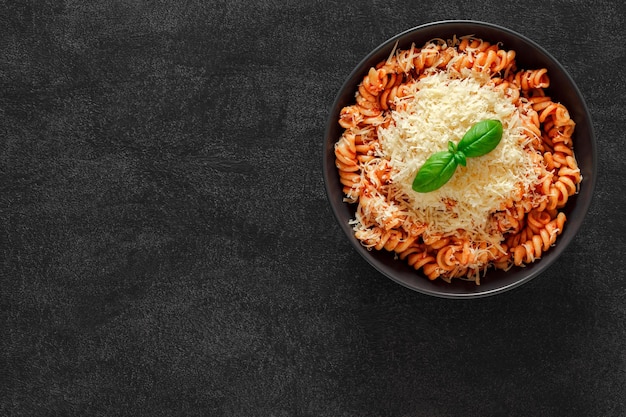 Fusilli pasta cooked with tomato sauce grated parmesan and basil on dark background top view space to copy text