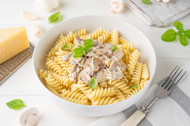 Fusilli pasta met champignons kaas en verse basilicum in een bord op een witte houten achtergrond