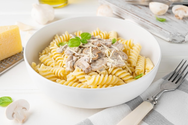 Fusilli pasta met champignons kaas en verse basilicum in een bord op een witte houten achtergrond