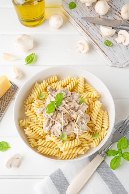 Fusilli pasta met champignons kaas en verse basilicum in een bord op een witte houten achtergrond