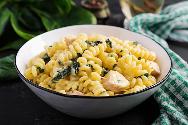 Fusilli pasta met een romige saus met kippenvlees parmesan kaas en spinazie op een schaal op een donkere achtergrond