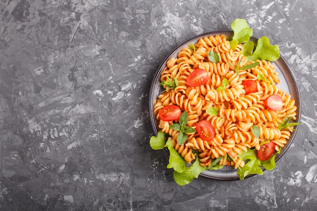 Fusilli pasta with tomato sauce cherry tomatoes lettuce and herbs on a black concrete background