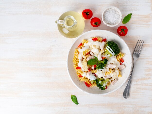 Fusilli van deegwaren met groenten, vlees, witte saus op witte houten