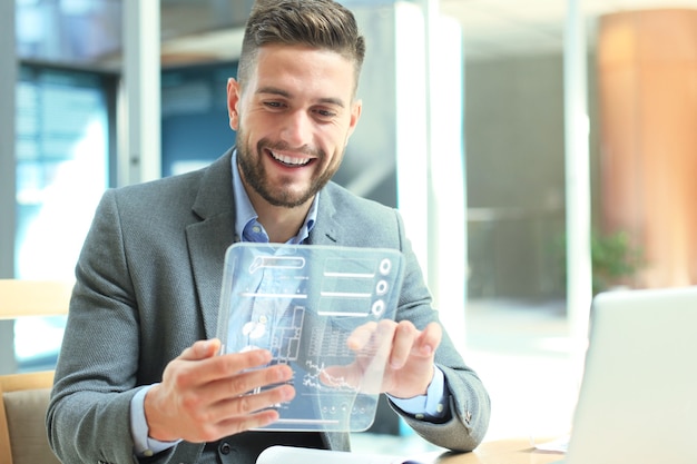 Future concept. Businessman analyzing financial statistics displayed on the futuristic transparent tablet screen.