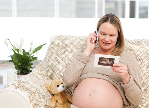 Future mom looking at an echography while phoning 