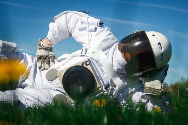 写真 ヘルメットをかぶった未来の宇宙飛行士は、花の間の緑の芝生に座っています。