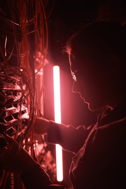 Futuristic shot of young network engineer working with server in red light, focus on profile outline