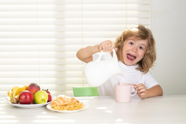 Fuuny excited little boy pouring whole cows milk for breakfast schoolkid eating breakfast before sch