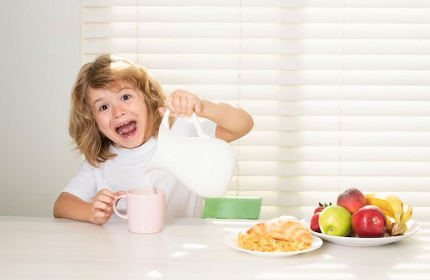 興奮した小さな男の子が朝食に牛乳を注ぐ 学生が朝食を食べる前に