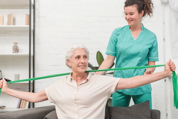 Foto fysiotherapeut die de oude vrouw helpen die zich met groene oefeningsband uitrekt