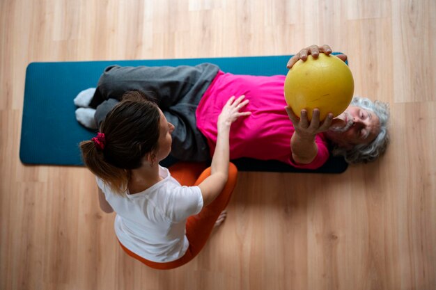 Foto fysiotherapeut die een oudere man helpt zich te rehabiliteren en actief te blijven