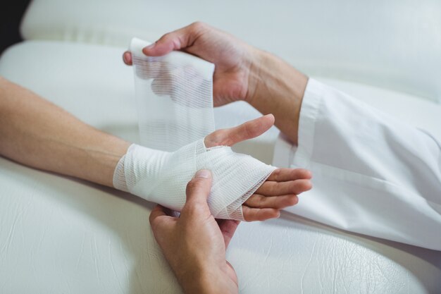 Fysiotherapeut die verband op verwonde hand van patiënt zet