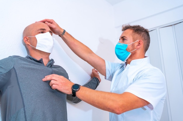 Fysiotherapeut met masker die de nek van de klant uitrekt met een haar op de muur Fysiotherapie met beschermende maatregelen in de Coronavirus pandemie COVID19 Osteopathie sport quiromassage