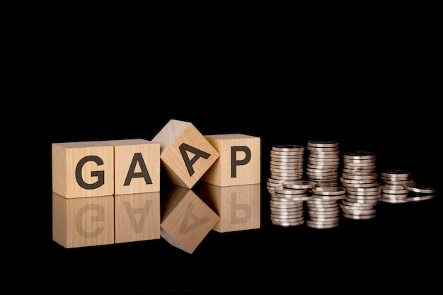 GAAP wooden cubes black background stacks with coins inscription on the cubes is reflected from the surface of the table GAAP short for Generally Accepted Accounting Principles