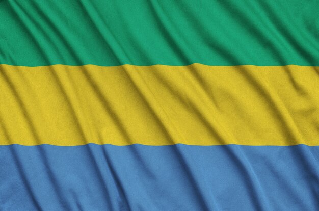 Gabon flag is depicted on a sports cloth fabric with many folds.