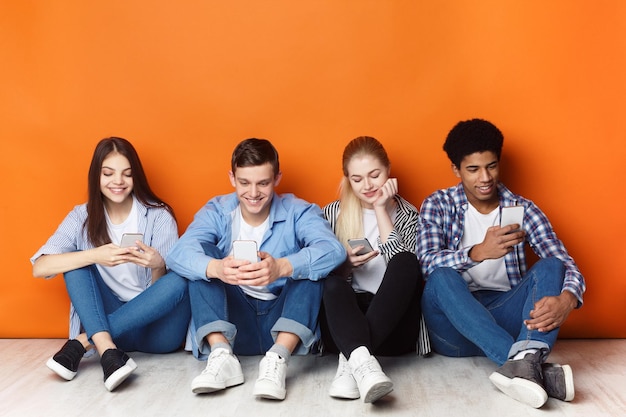Foto dipendenza da gadget adolescenti con smartphone parete arancione