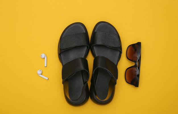 Gadgets and women's accessories on yellow background. Sandals, headphones and sunglasses. Top view. Flat lay