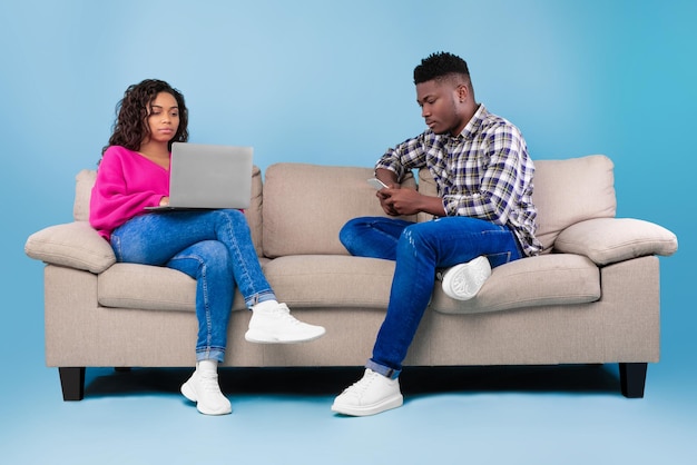 Gadgetverslaving Afro-Amerikaanse man en vrouw zittend op de bank met behulp van mobiele telefoon en laptop op