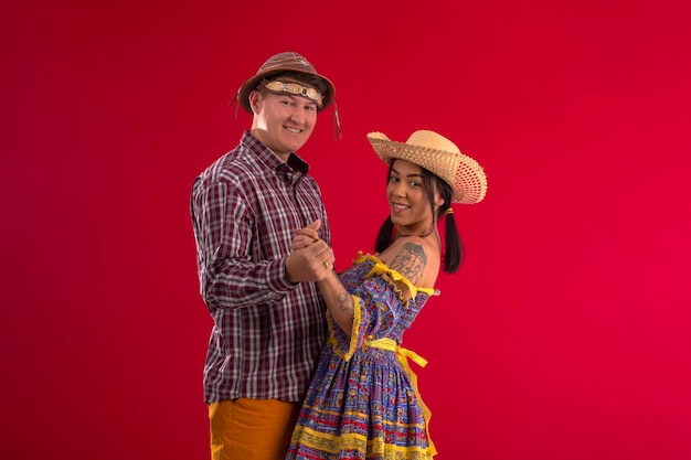 Gama Federal District Brazil May 29 2022 Young couple wearing festive costumes in studio photo with red background and fun poses Festa Junina Brazil