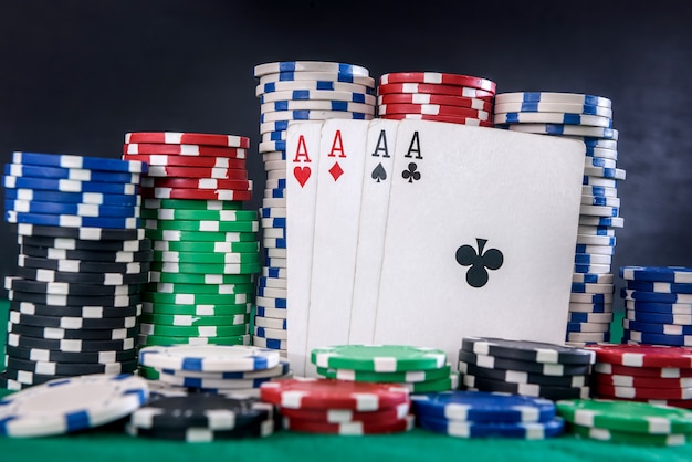 ギャンブルの概念。緑のテーブルのポーカーチップと4つのエースの組み合わせ
