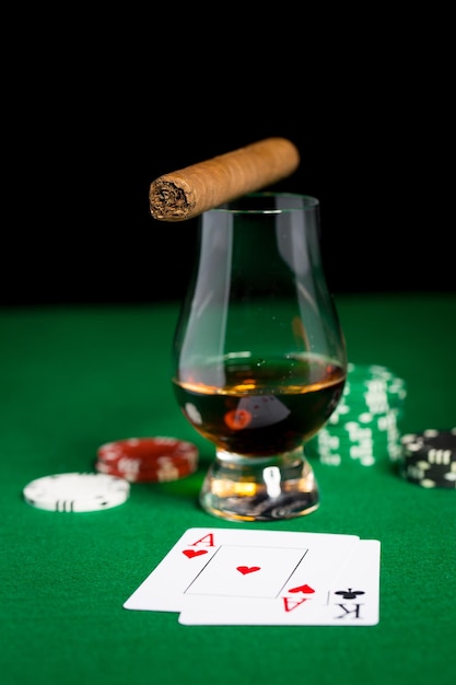 gambling, fortune and entertainment concept - close up of casino chips, whisky glass, playing cards and cigar on green table surface