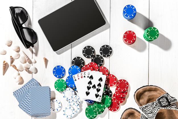 Gambling. Poker chips, cards and the dice nearby tablet on white wooden table. Top view. Copyspace. Poker. Summer