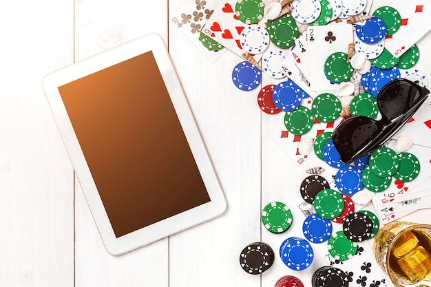 Gambling poker chips cards and the dice nearby tablet on wooden table top view copyspace poker