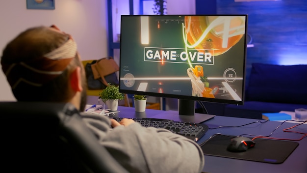 Game over per il giocatore sconvolto che gioca su un potente gioco sparatutto in prima persona per computer durante il torneo online. uomo sconfitto con le cuffie in streaming cyber online che si esibisce a tarda notte nella sala da gioco