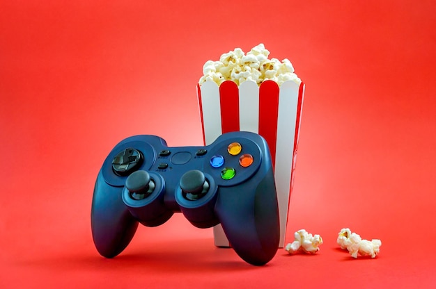 Gamepad en popcorn in een gestreepte papieren beker op een rode achtergrond Gaming-vrijetijds- en entertainmentconcept