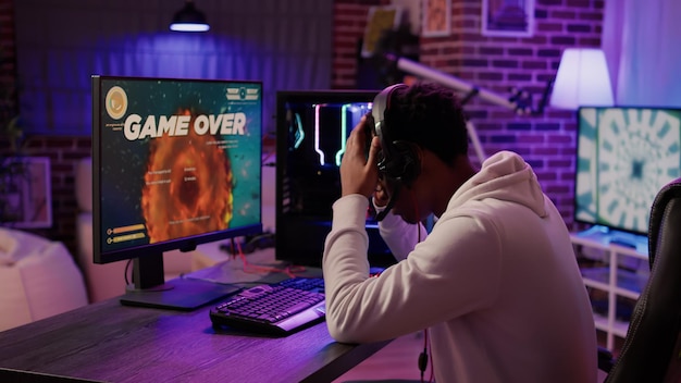 Gamer feeling unhappy after losing difficult level in online\
space shooter on gaming pc at home. african american man playing\
internet multiplayer game disappointed after failing\
competition.