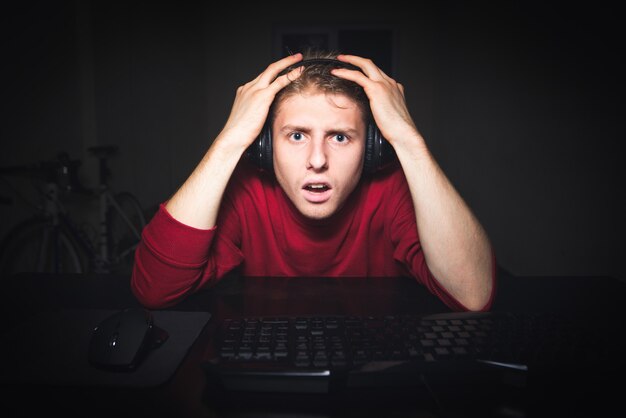 Gamer in the headphones sits at night in  room of home