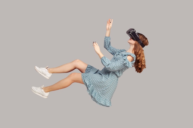 Gamer-meisje in jurk zweeft in de lucht, zweeft met een virtual reality-bril op het hoofd, speelt vr