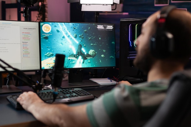 Gamer playing video games on stream with live chat. Man using microphone and headset on computer, live streaming gameplay online. Streamer broadcasting with gaming equipment at monitor.