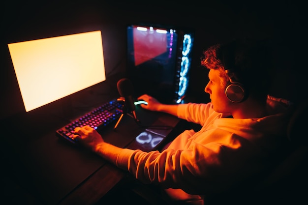 Gamer sits at night at a table with a microphone and headphones looks at red screen and plays games