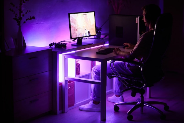Giocatore seduto al tavolo davanti al monitor del computer e giocare al computer in camera oscura a casa