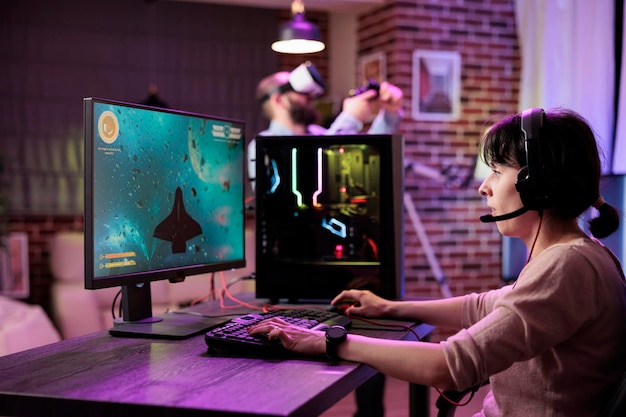 gamer using professional grade level gaming setup to avoid disruptive lag while playing esports tournaments. woman relaxing in rgb lights apartment playing action shooting videogame late at night