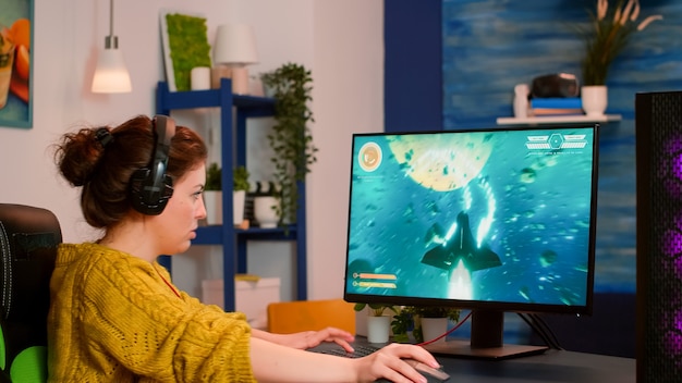 Gamer woman with headphones relaxing at home playing space shooter video game on powerful computer