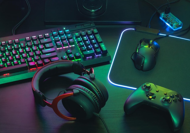 Foto gamer concept di spazio di lavoro vista superiore di un'attrezzatura da gioco topo tastiera joystick auricolare joystick mobile in orecchio cuffie e mouse pad con colore rgb su sfondo nero tavolo