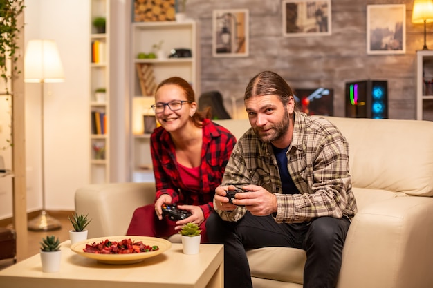 Gamers couple playing video games on the TV with wireless controllers in hands.